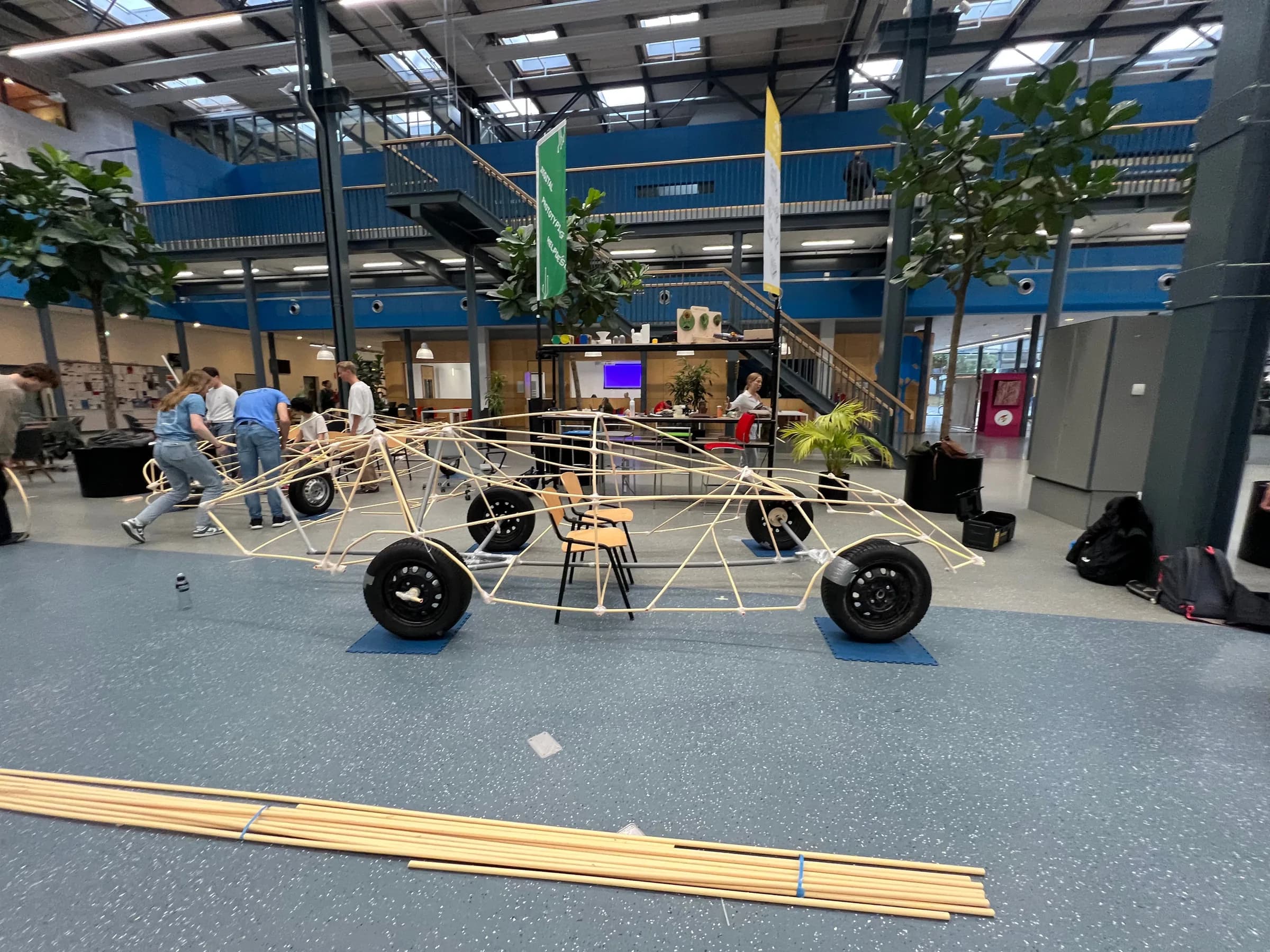 Het voltooide lattenframe van de PVC-car op wielen in de projecthal, met het team eromheen